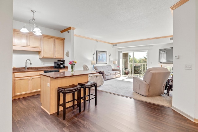 kitchen featuring a sink, open floor plan, light brown cabinetry, a center island, and ornamental molding