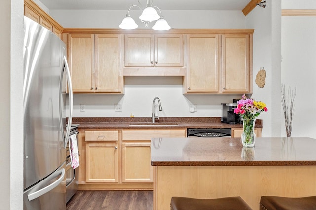 kitchen featuring appliances with stainless steel finishes, a sink, light brown cabinetry, dark stone countertops, and decorative light fixtures