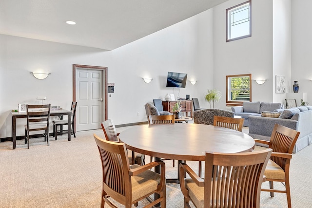 dining room with plenty of natural light, light carpet, a towering ceiling, and baseboards