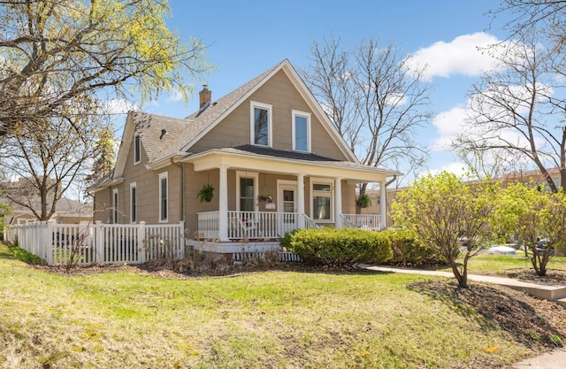 country-style home featuring a shingled roof, a front yard, covered porch, and a chimney