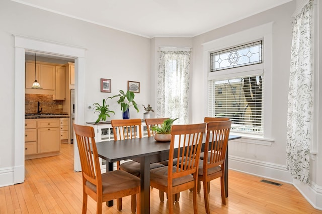 dining room featuring baseboards, visible vents, ornamental molding, and light wood-style floors
