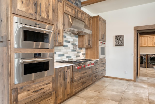 kitchen with under cabinet range hood, brown cabinetry, decorative backsplash, washer and clothes dryer, and appliances with stainless steel finishes