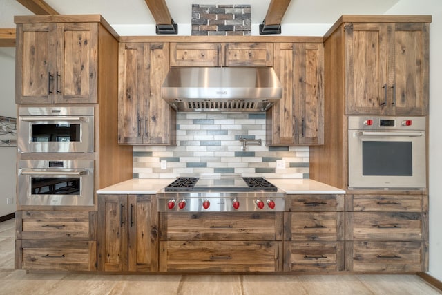 kitchen with under cabinet range hood, stainless steel appliances, brown cabinets, and backsplash