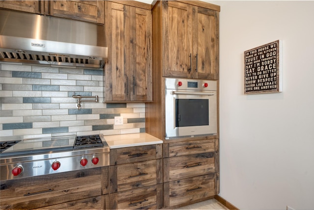 kitchen with under cabinet range hood, stainless steel appliances, tasteful backsplash, and brown cabinetry