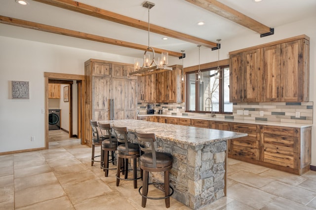 kitchen featuring washer / clothes dryer, a center island, a sink, decorative backsplash, and brown cabinets