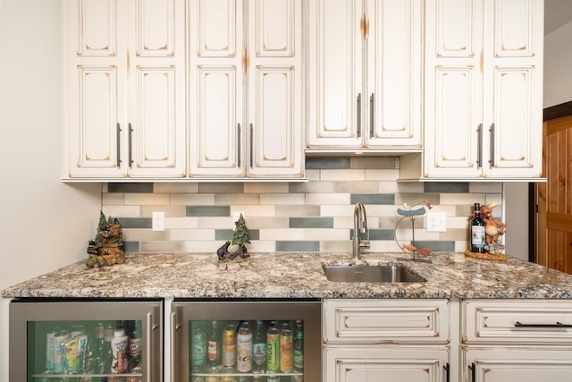 kitchen featuring beverage cooler, decorative backsplash, light stone counters, and a sink