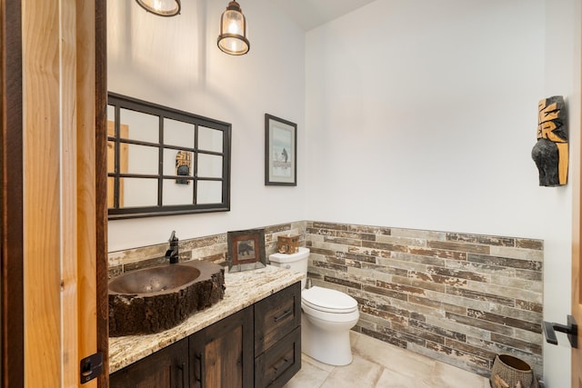 bathroom with vanity, toilet, a wainscoted wall, and tile patterned floors