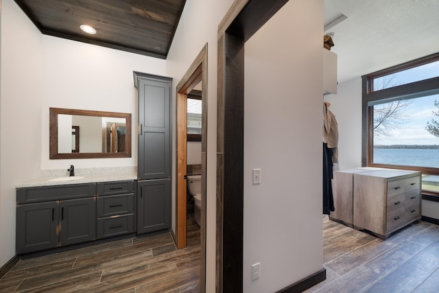 corridor featuring recessed lighting, dark wood-type flooring, baseboards, and a sink