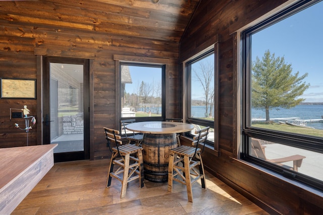 sunroom / solarium featuring lofted ceiling, wood walls, wood ceiling, wood finished floors, and a water view