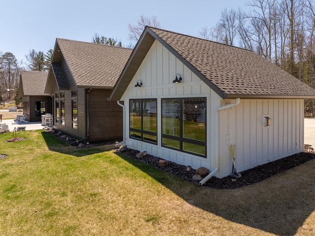 back of house featuring a lawn, board and batten siding, and a shingled roof