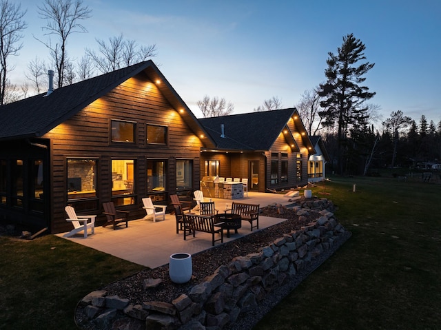 rear view of property with a yard, roof with shingles, a patio area, and an outdoor fire pit