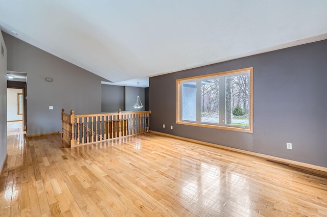 empty room with hardwood / wood-style flooring, visible vents, baseboards, and lofted ceiling