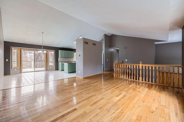 unfurnished living room with visible vents, a chandelier, light wood-style flooring, and lofted ceiling