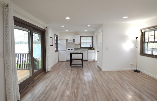 interior space featuring baseboards, light wood finished floors, white cabinets, and white appliances