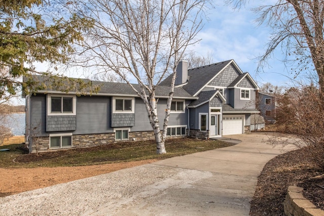 view of front facade featuring an attached garage, a chimney, driveway, and stone siding