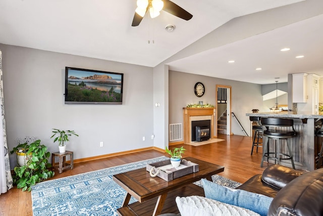 living area with a ceiling fan, vaulted ceiling, wood finished floors, and visible vents