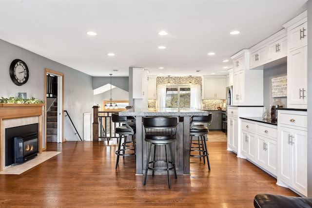 kitchen with white cabinets, dark wood-style flooring, a kitchen breakfast bar, recessed lighting, and backsplash