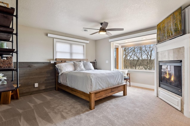 bedroom featuring a tiled fireplace, carpet floors, multiple windows, and a textured ceiling