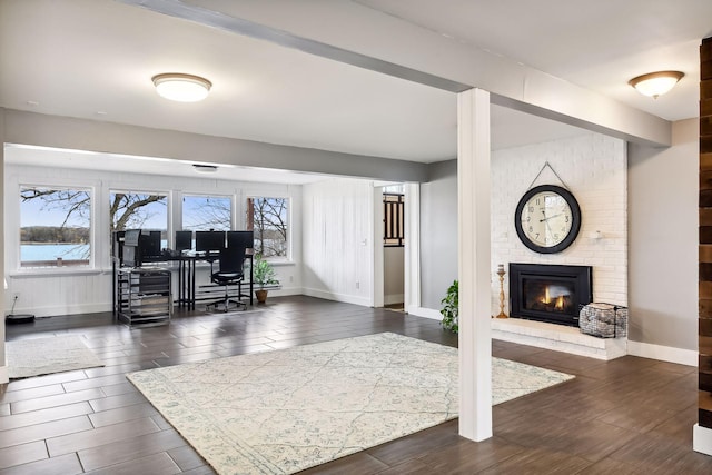 living room with baseboards, dark wood-style flooring, and a brick fireplace