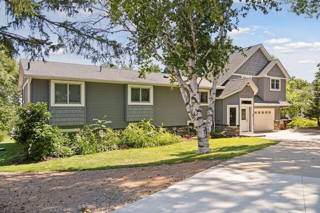 view of front facade with a garage, concrete driveway, a front yard, and stone siding
