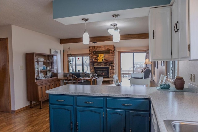 19447 County Road 1, Morris, MN 56267 - kitchen with blue cabinets, a peninsula, light wood-style flooring, a fireplace, and beamed ceiling
