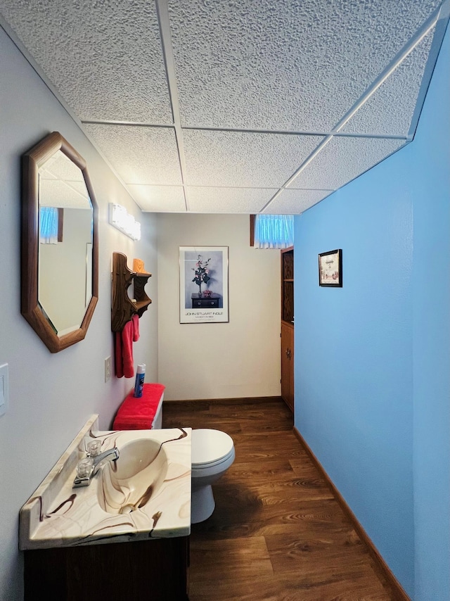 19447 County Road 1, Morris, MN 56267 - half bathroom featuring a drop ceiling, toilet, vanity, wood finished floors, and baseboards
