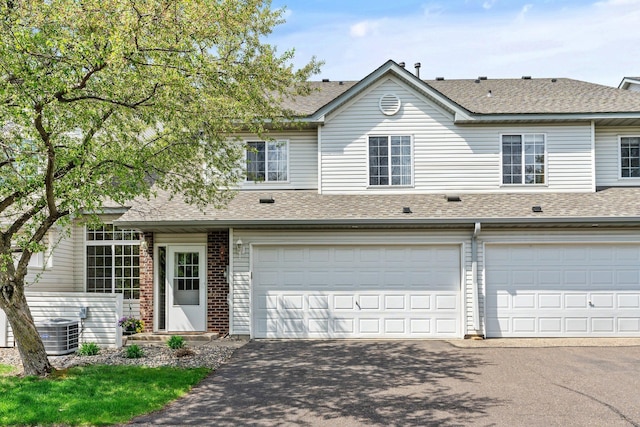 view of property with a shingled roof, asphalt driveway, a garage, and central AC unit