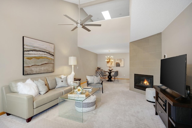 carpeted living room with a fireplace, a ceiling fan, baseboards, high vaulted ceiling, and a chandelier