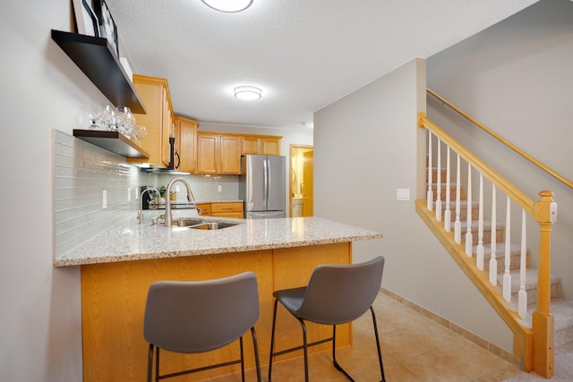 kitchen with freestanding refrigerator, a sink, a peninsula, tasteful backsplash, and light stone countertops