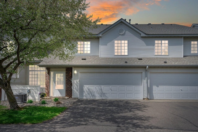 townhome / multi-family property with driveway, a garage, and a shingled roof