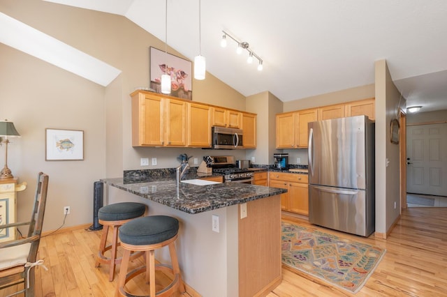 kitchen with light brown cabinetry, dark stone counters, stainless steel appliances, a peninsula, and light wood-type flooring
