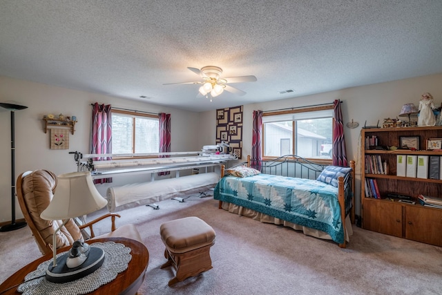 carpeted bedroom featuring a textured ceiling, visible vents, a ceiling fan, and multiple windows
