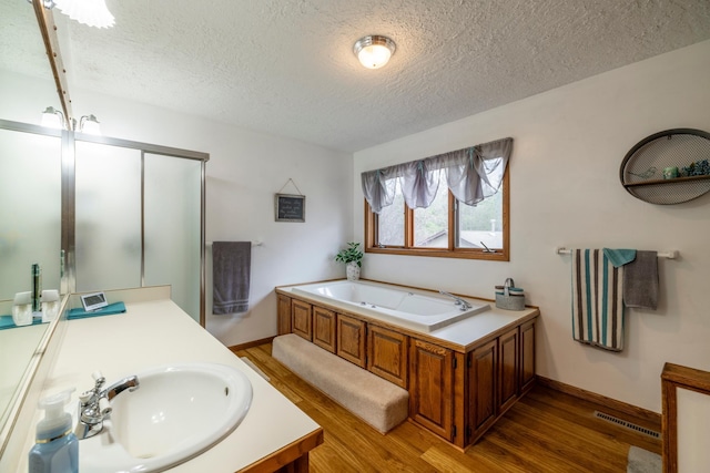 full bath featuring a bath, a textured ceiling, and wood finished floors