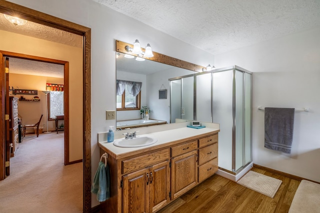 full bath featuring a textured ceiling, a shower stall, baseboards, wood finished floors, and vanity