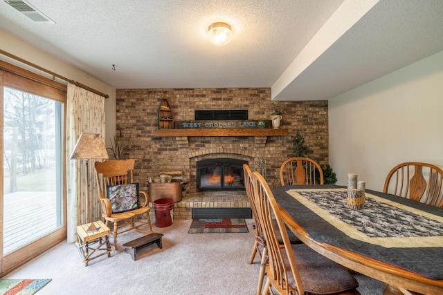 dining space featuring a brick fireplace, a textured ceiling, visible vents, and carpet floors