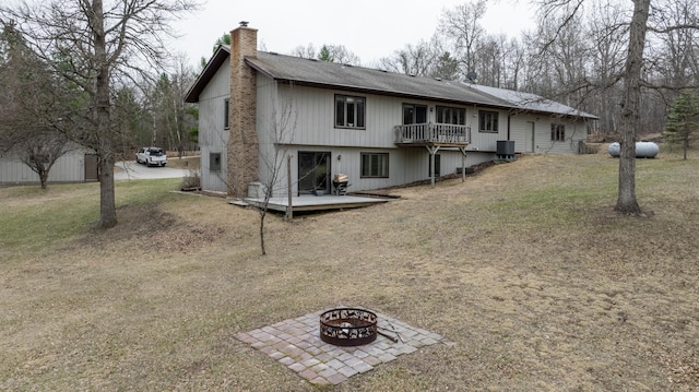 back of property featuring a chimney, a deck, an outdoor fire pit, a lawn, and central AC