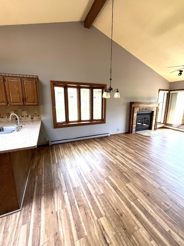 unfurnished living room featuring a sink, baseboard heating, a fireplace, light wood-type flooring, and beamed ceiling