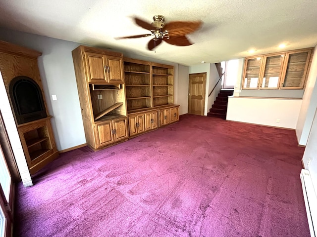 unfurnished living room with baseboard heating, stairway, a ceiling fan, dark carpet, and built in features