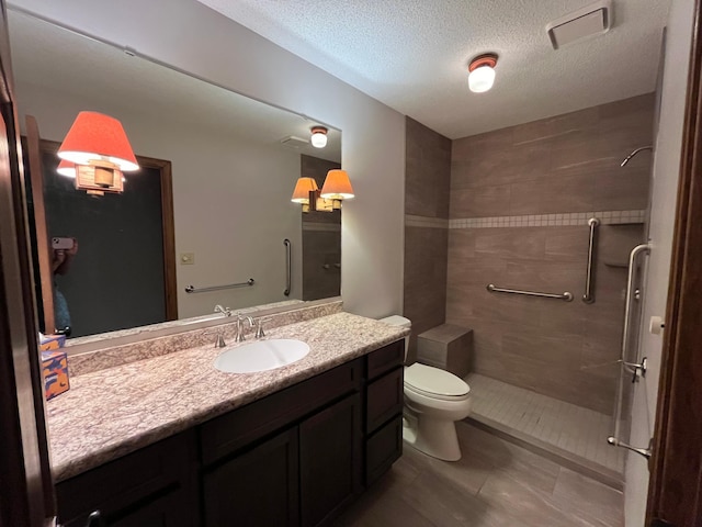 full bath featuring tile patterned floors, toilet, vanity, tiled shower, and a textured ceiling