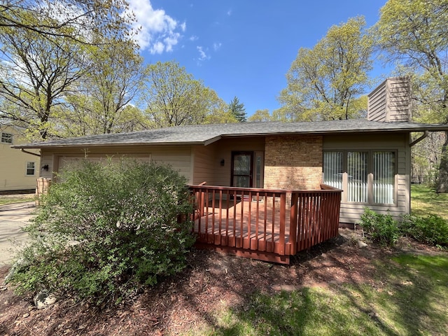 back of house featuring an attached garage, a chimney, a wooden deck, and brick siding