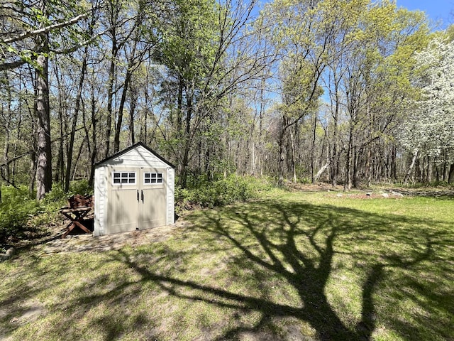view of grassy yard with a shed, an outdoor structure, and a wooded view