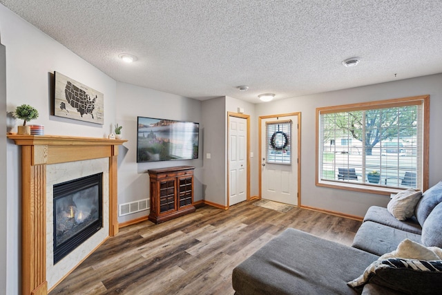 living room featuring a textured ceiling, a tiled fireplace, baseboards, wood finished floors, and visible vents