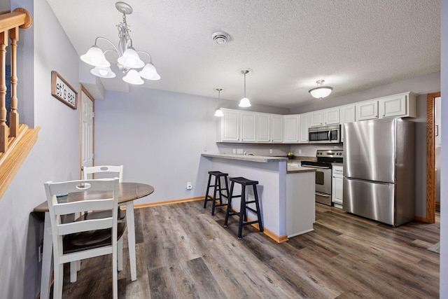 kitchen with a peninsula, a kitchen breakfast bar, white cabinetry, a chandelier, and stainless steel appliances