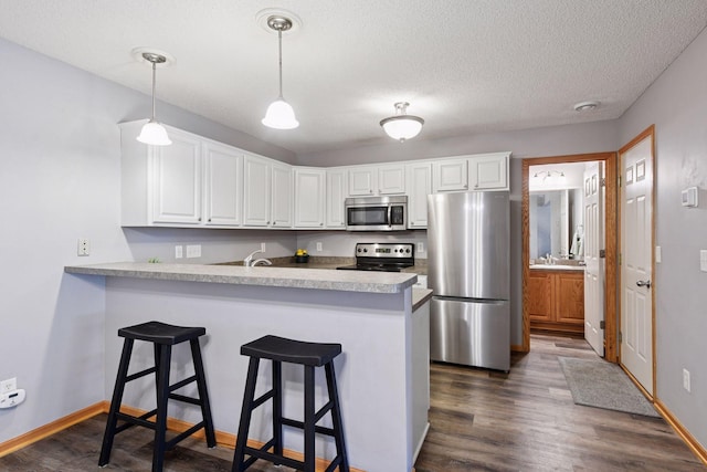 kitchen with white cabinets, stainless steel appliances, dark wood finished floors, and a peninsula