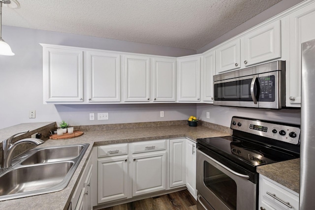 kitchen featuring a textured ceiling, appliances with stainless steel finishes, a sink, dark wood-style floors, and white cabinetry