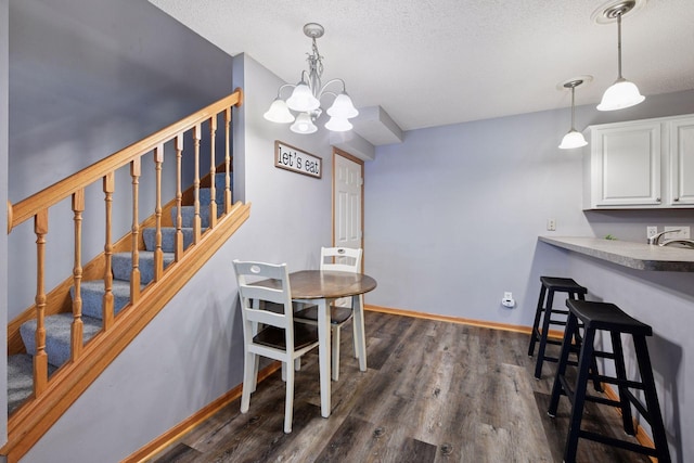 dining room featuring a notable chandelier, a textured ceiling, dark wood finished floors, baseboards, and stairway