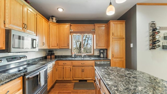 kitchen featuring pendant lighting, dark stone counters, a sink, appliances with stainless steel finishes, and dark wood finished floors