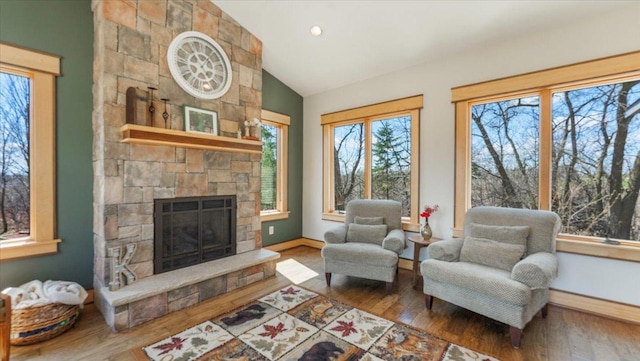 interior space with baseboards, hardwood / wood-style flooring, a stone fireplace, and lofted ceiling