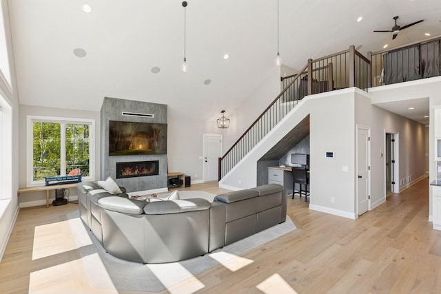 1929 Fagerness Point Rd, Orono, MN 55391 - living area with high vaulted ceiling, stairway, a tiled fireplace, light wood finished floors, and baseboards