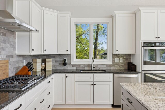 1929 Fagerness Point Rd, Orono, MN 55391 - kitchen with wall chimney range hood, stainless steel appliances, a sink, and dark stone counters